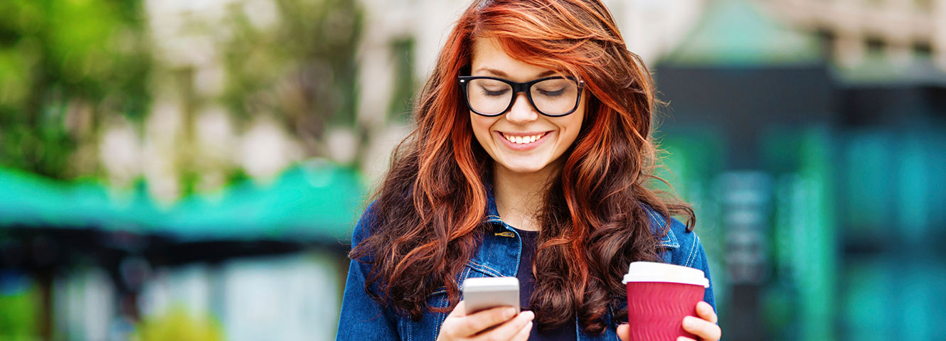 Woman holding coffee and phone outdoors.