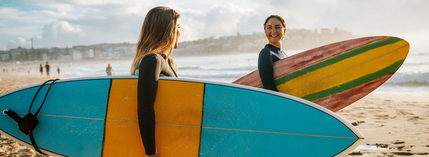 Two woman holding surf boards.